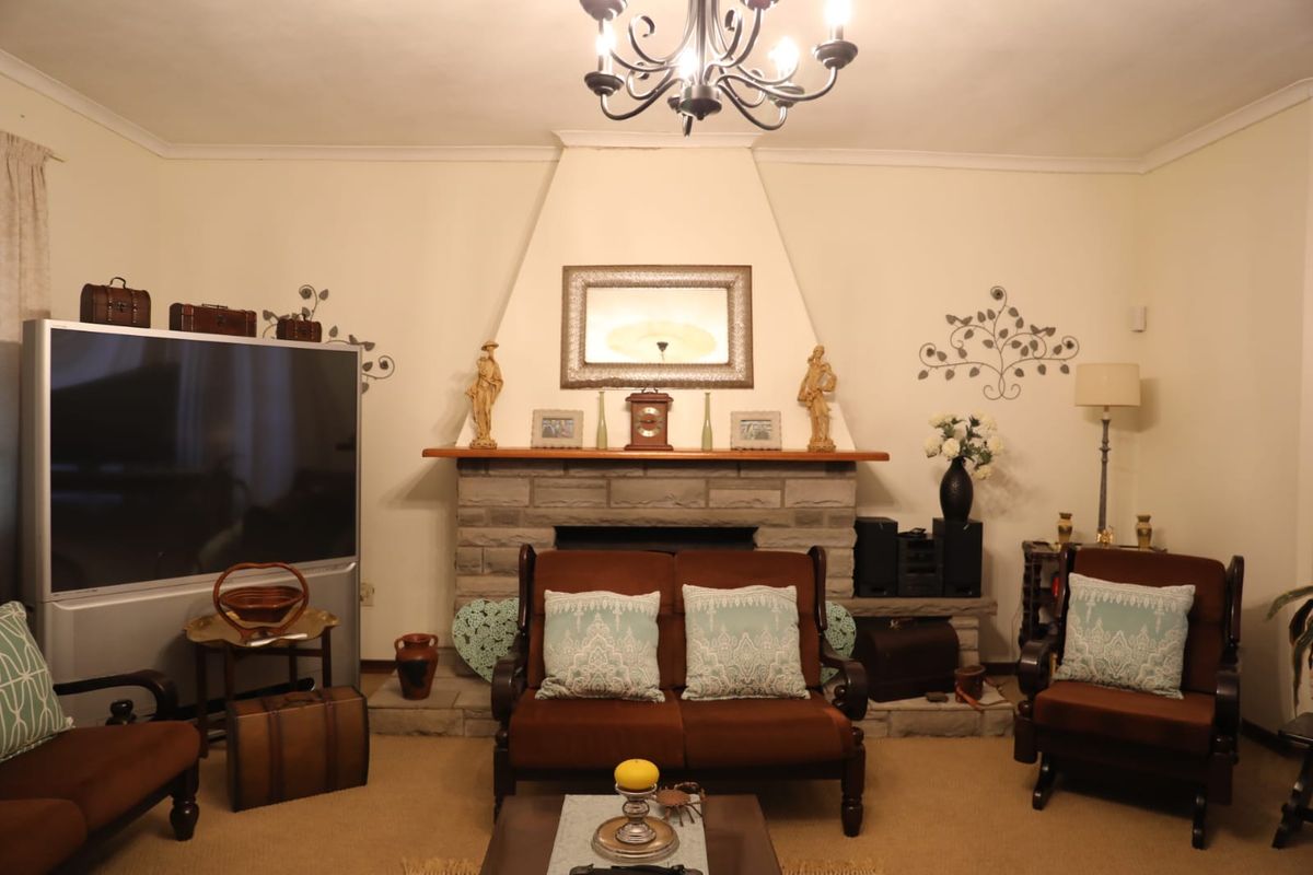A cozy living room featuring a prominent stone fireplace with a wooden mantelpiece and a decorative ceiling chandelier.