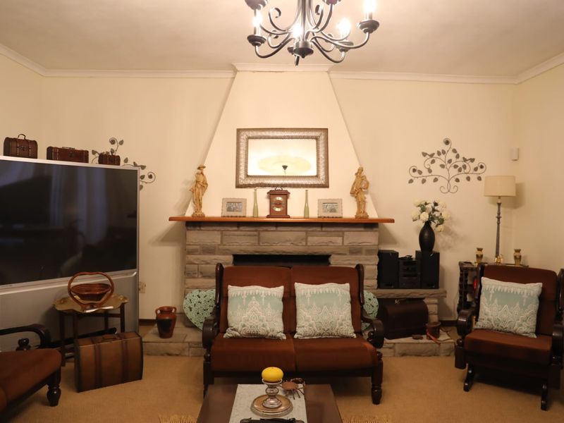 A cozy living room featuring a prominent stone fireplace with a wooden mantelpiece and a decorative ceiling chandelier.