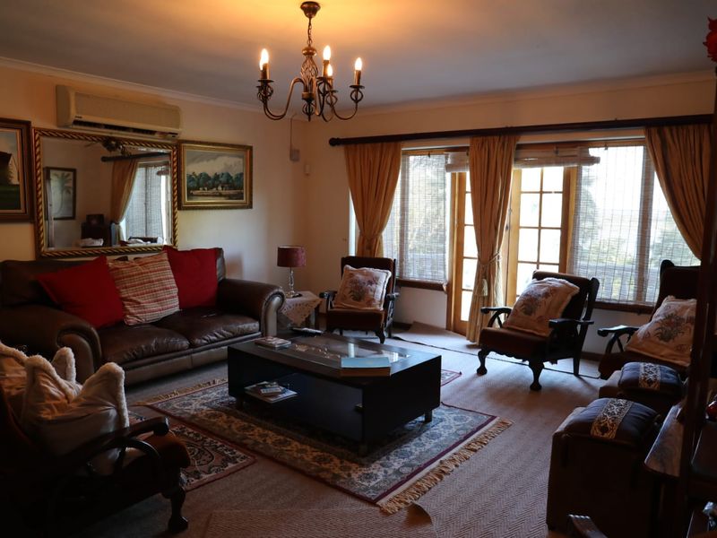 A comfortable living room featuring carpeted flooring, a central chandelier, wall-mounted air conditioning, and direct access to the outdoors through glass french doors.