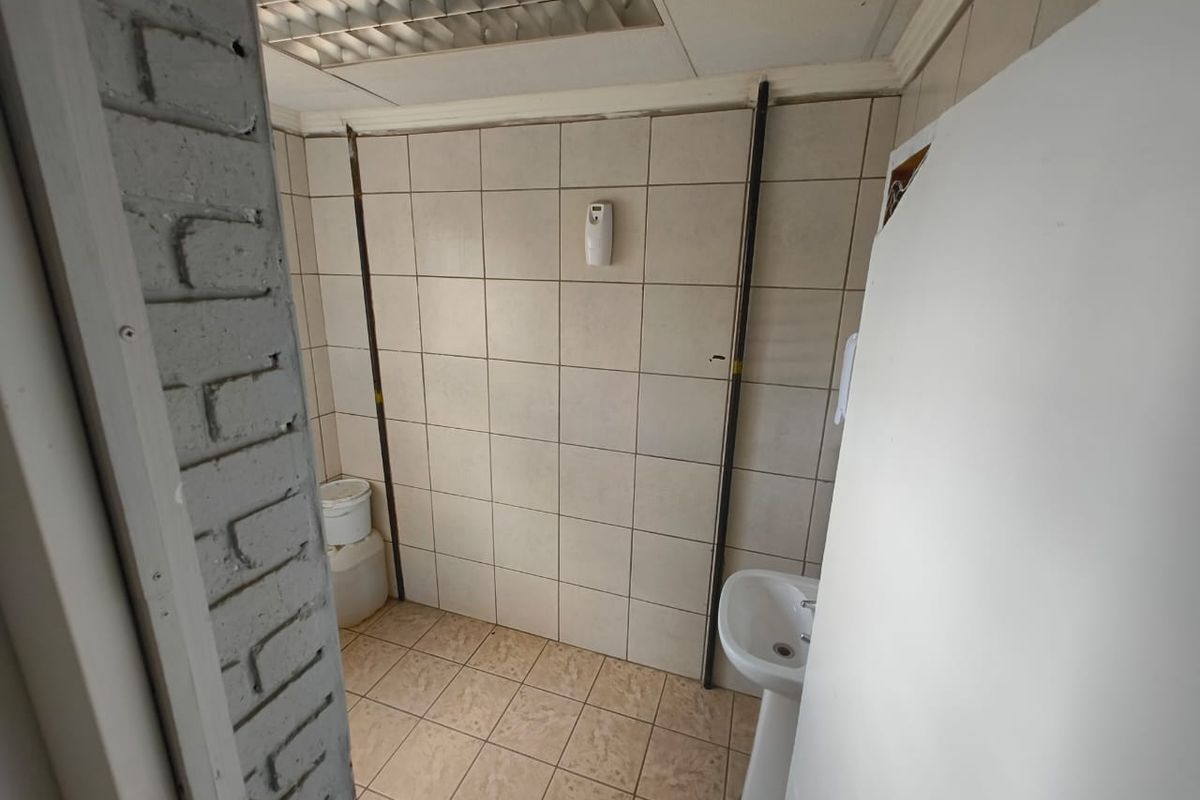 A functional commercial restroom featuring a pedestal basin, tiled walls, and a drop-in ceiling grid with integrated lighting.