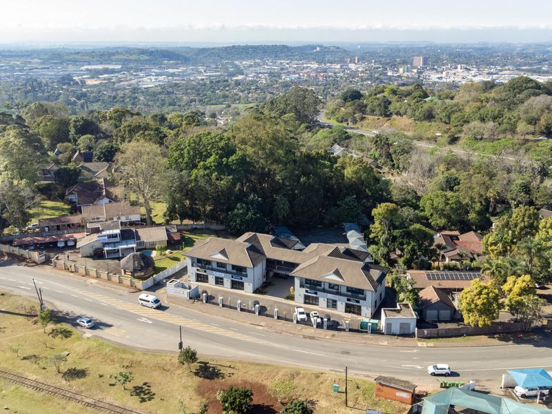 Aerial view of the office property featuring a multi-unit building with tiled roofing, paved parking, and perimeter security fencing in a suburban setting.
