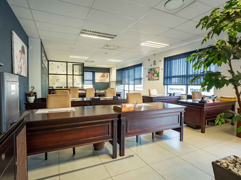 A professional open-plan office space featuring ceramic floor tiles, a suspended ceiling with recessed lighting, and large windows with vertical blinds.
