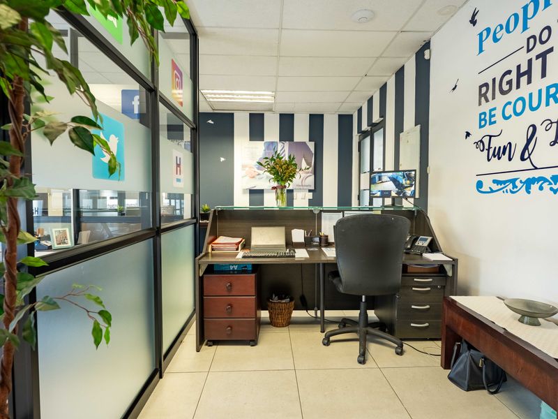 A professional office reception area featuring a built-in desk, glass partition walls, and modern tiled flooring with a suspended ceiling.