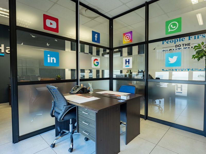 A professional office space featuring modern glass partition walls, recessed lighting, and clean tiled flooring, creating a bright and collaborative work environment.