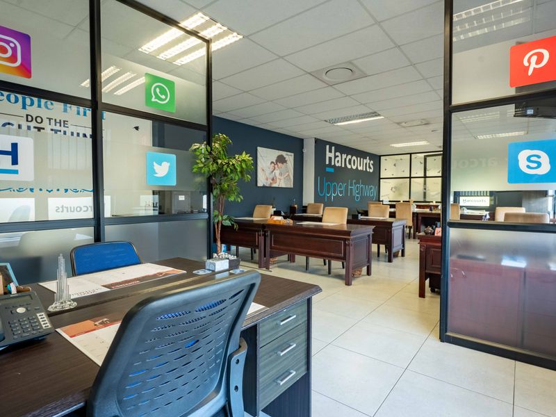 A professional open-plan office space featuring glass partitions, tiled flooring, and a suspended ceiling with recessed lighting.