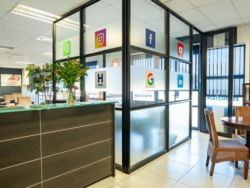 Professional office space featuring a modern reception desk, glass-partitioned meeting areas, suspended ceilings, and tiled flooring with integrated vertical blinds.