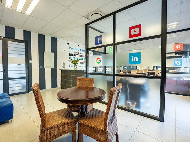 Modern office reception area featuring a built-in desk, tiled flooring, and a glass partition wall with branding decals.