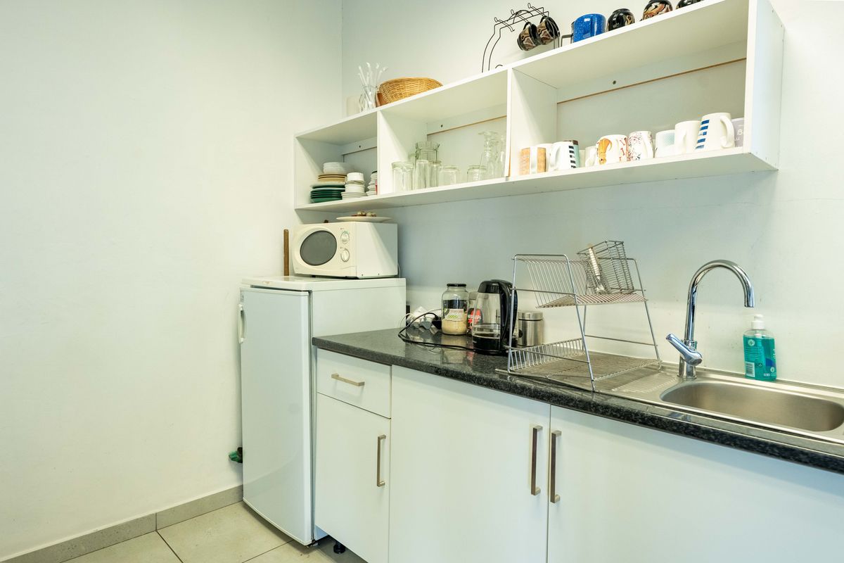 A compact office kitchenette featuring white cabinetry, open shelving, a stainless steel sink, and a dark laminate countertop.