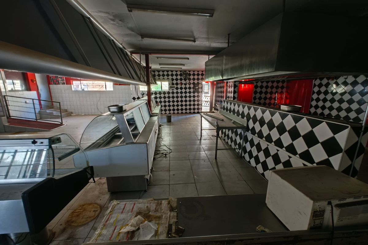 A vacant commercial kitchen space featuring built-in stainless steel counters, large extractor hoods, and checkered wall tiling, requiring significant refurbishment.