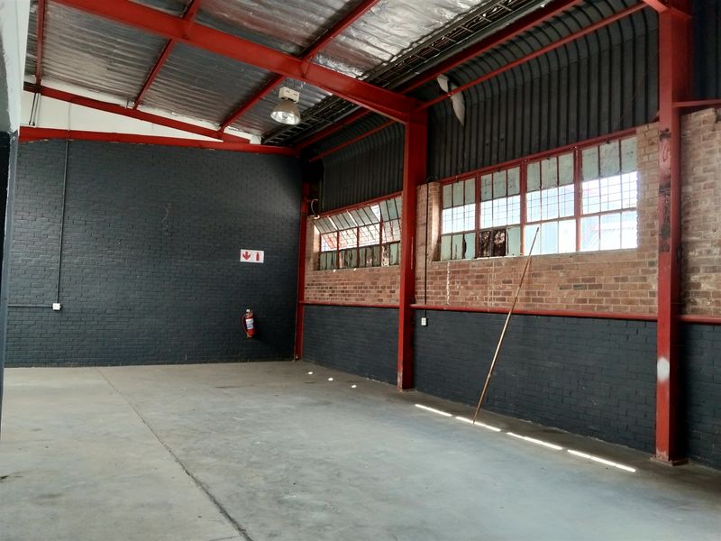 Spacious industrial utility area featuring exposed steel beams, concrete flooring, and large windows, suitable for workshop or storage use.
