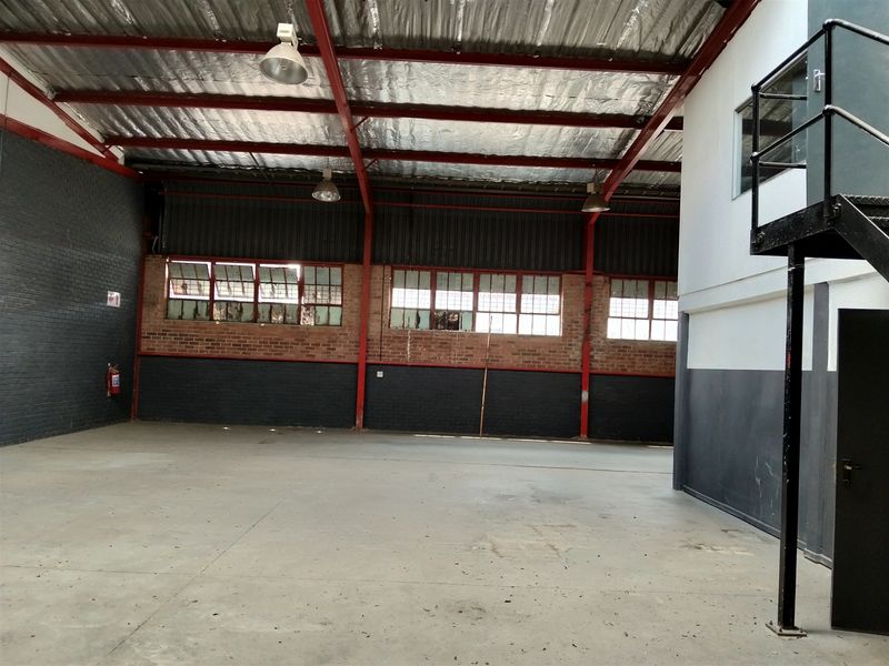 Spacious industrial warehouse unit featuring exposed steel roof trusses, concrete flooring, brick walls, and a mezzanine access staircase.