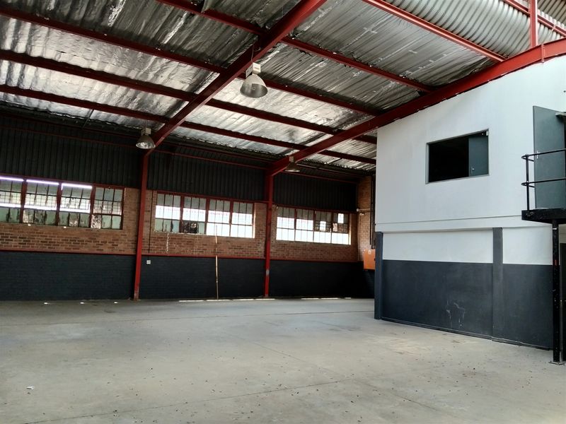 Spacious industrial warehouse unit featuring high exposed steel trusses, concrete flooring, and large steel-framed windows providing ample natural light.
