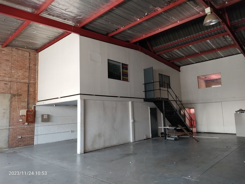 Spacious industrial warehouse unit featuring a mezzanine level, exposed steel roof structure, concrete flooring, and a functional metal staircase.