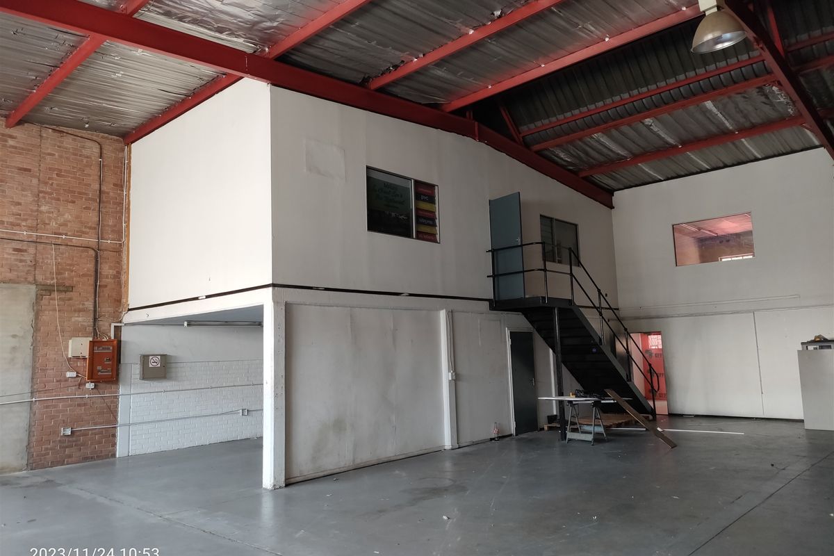 Spacious industrial warehouse unit featuring a mezzanine level, exposed steel roof structure, concrete flooring, and a functional metal staircase.