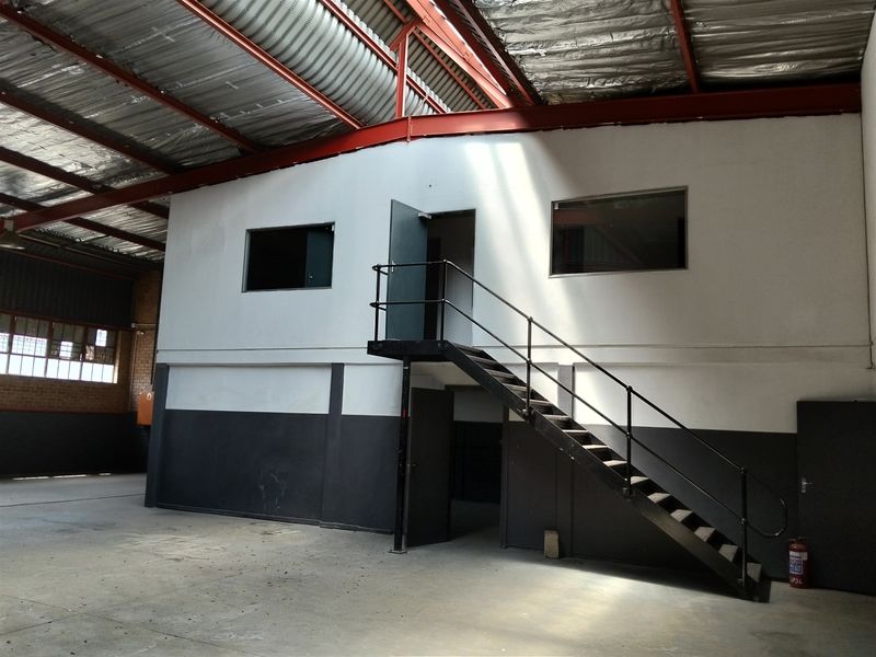 Spacious industrial warehouse unit featuring a mezzanine level with staircase access, exposed steel roof structure, and durable concrete flooring.