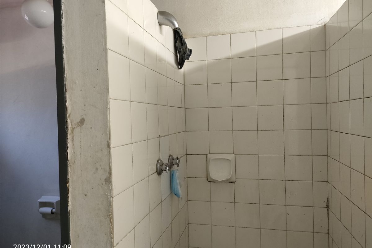 A dated shower enclosure featuring white ceramic wall tiles, a built-in soap dish, and standard shower fixtures, requiring maintenance and cosmetic updates.