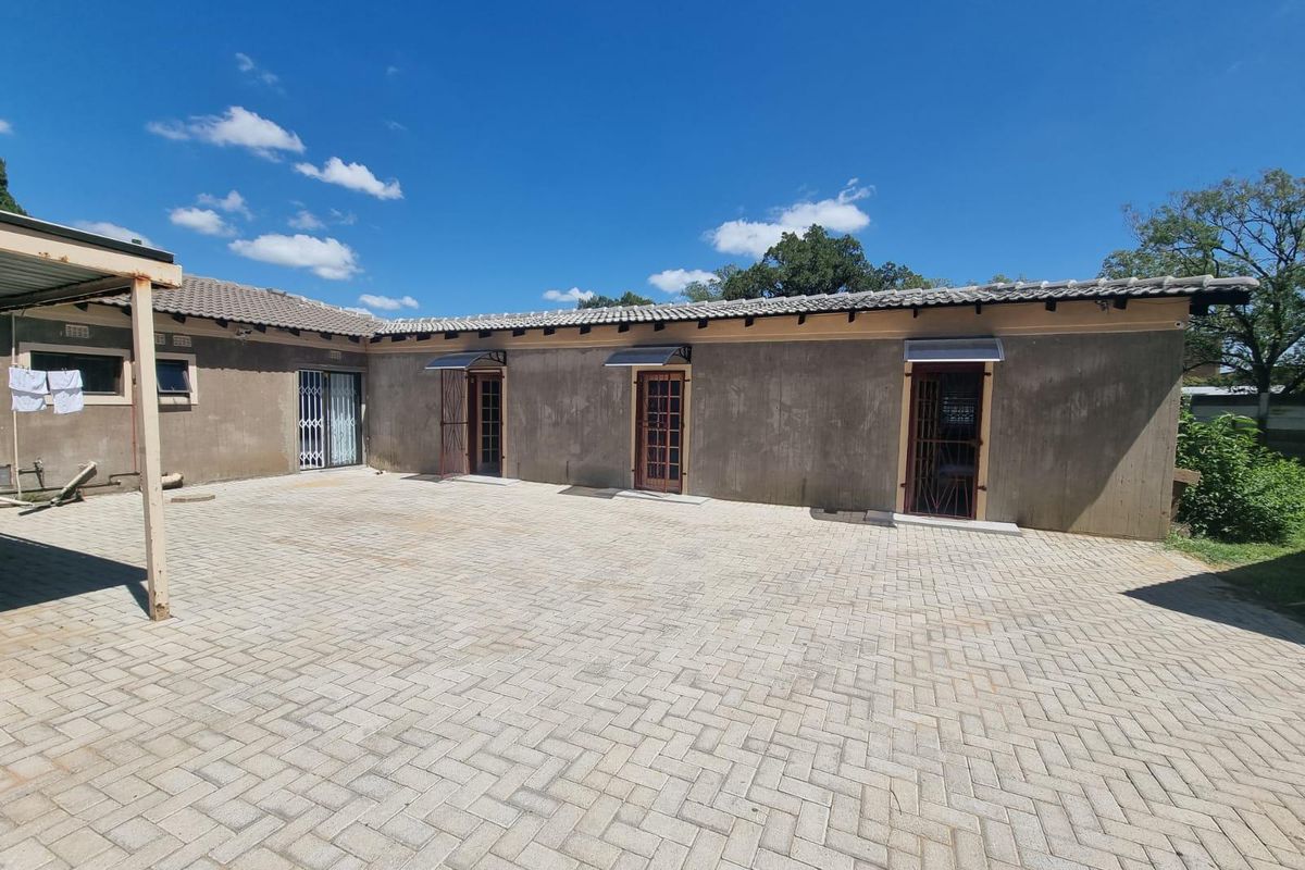 Rear exterior view of the guest house featuring a large paved courtyard, multiple access doors with security gates, and tiled roof structure.
