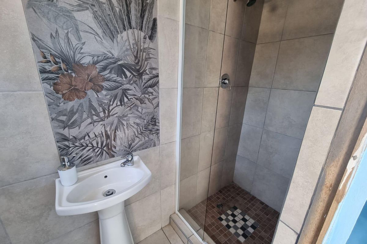 A compact bathroom featuring a pedestal basin with decorative wall tiling and a glass-enclosed shower with mosaic floor detailing.