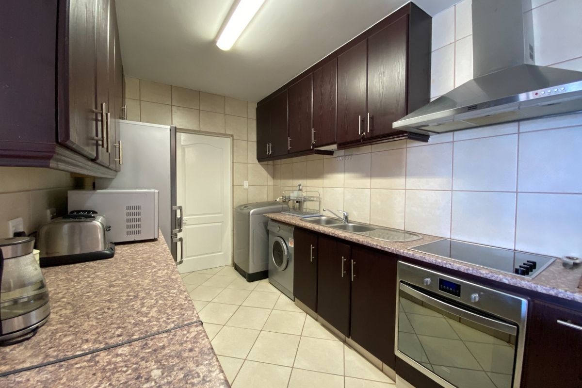 A functional kitchen featuring dark wood cabinetry, tiled backsplash, built-in oven, hob, extractor fan, and integrated laundry appliance space.