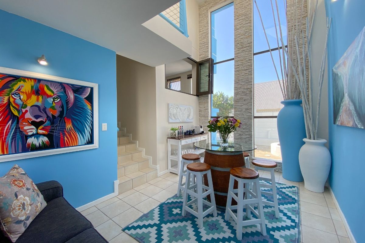 A bright, double-volume living area featuring floor-to-ceiling windows, tiled flooring, and a staircase leading to the upper level.