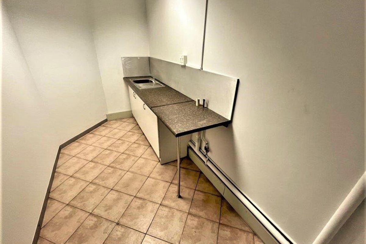 A compact kitchenette area featuring a single sink, laminate countertop, and base cabinetry, suitable for office utility or breakroom use.