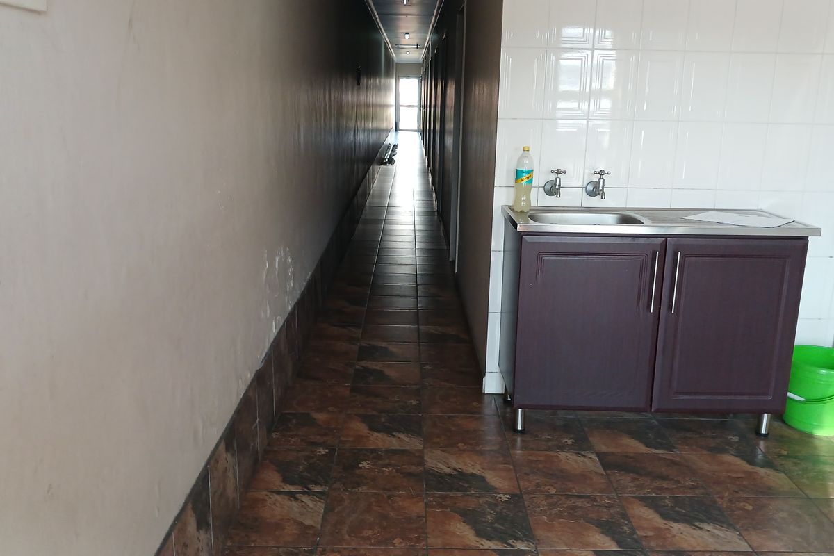 A long office hallway featuring tiled flooring and a small built-in sink station with wall tiling.