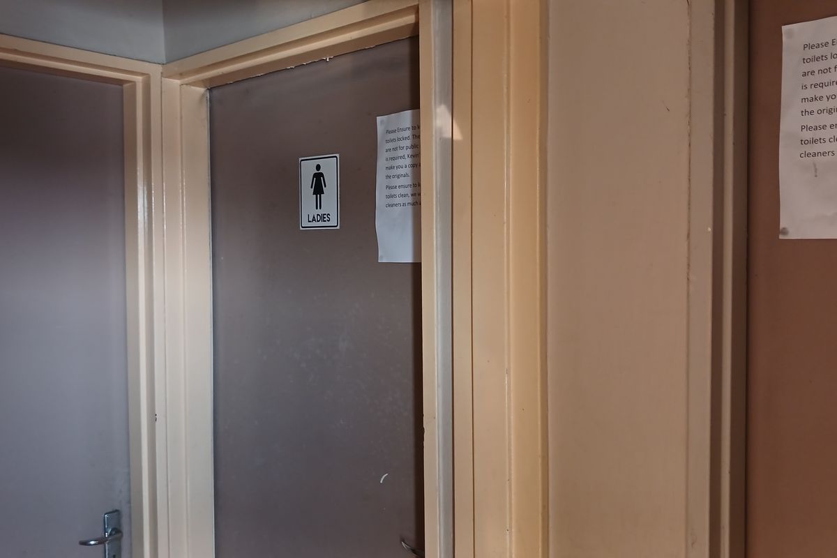 A hallway view showing the entrance to a ladies restroom with signage and paper notices attached to the doors.
