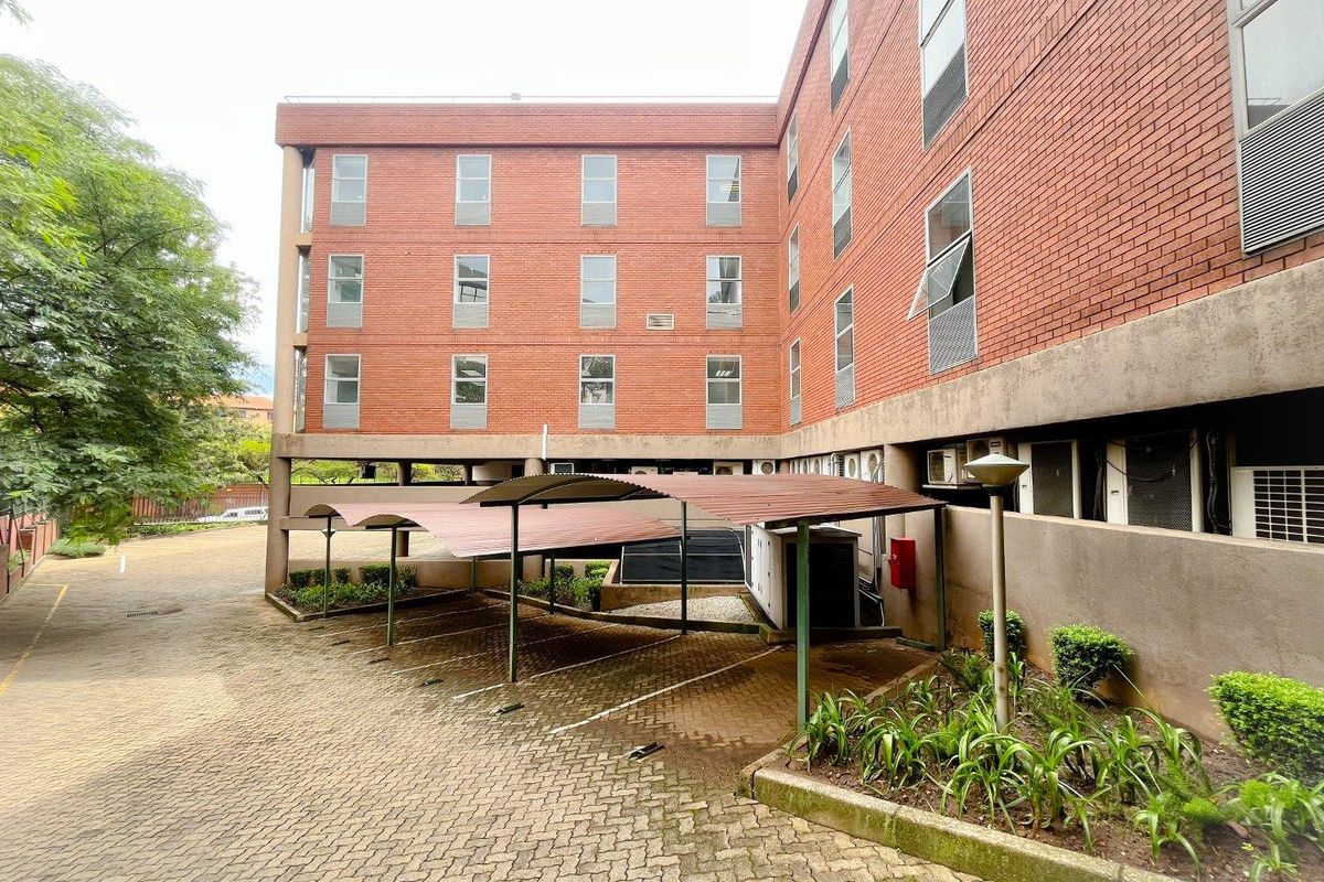 Exterior view of a multi-story brick office building featuring covered parking bays and paved driveway access.