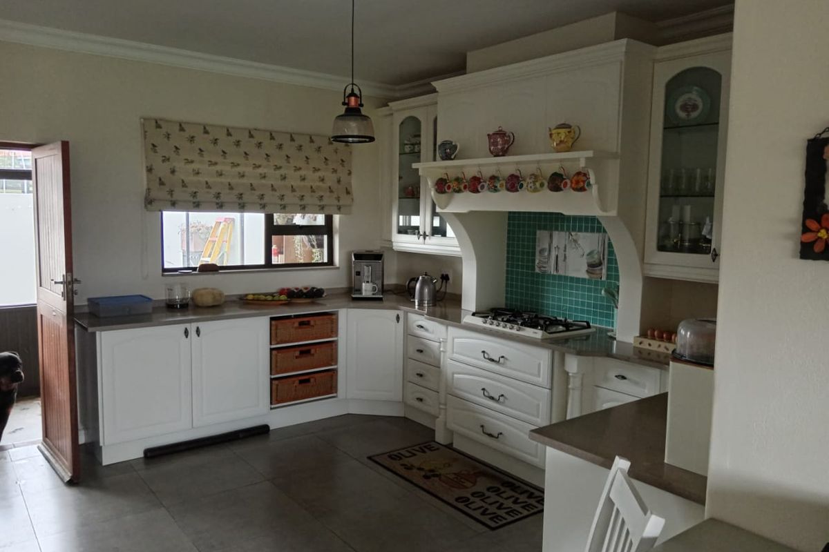 A well-maintained kitchen featuring white cabinetry, stone countertops, a gas hob with a decorative extractor hood, and tiled flooring.