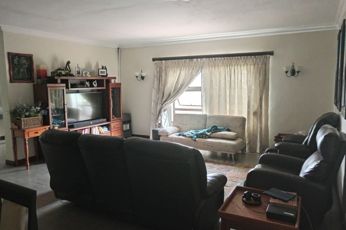 A living room featuring tiled flooring, wall-mounted lighting, and a large window with curtains. Note visible water staining on the ceiling.