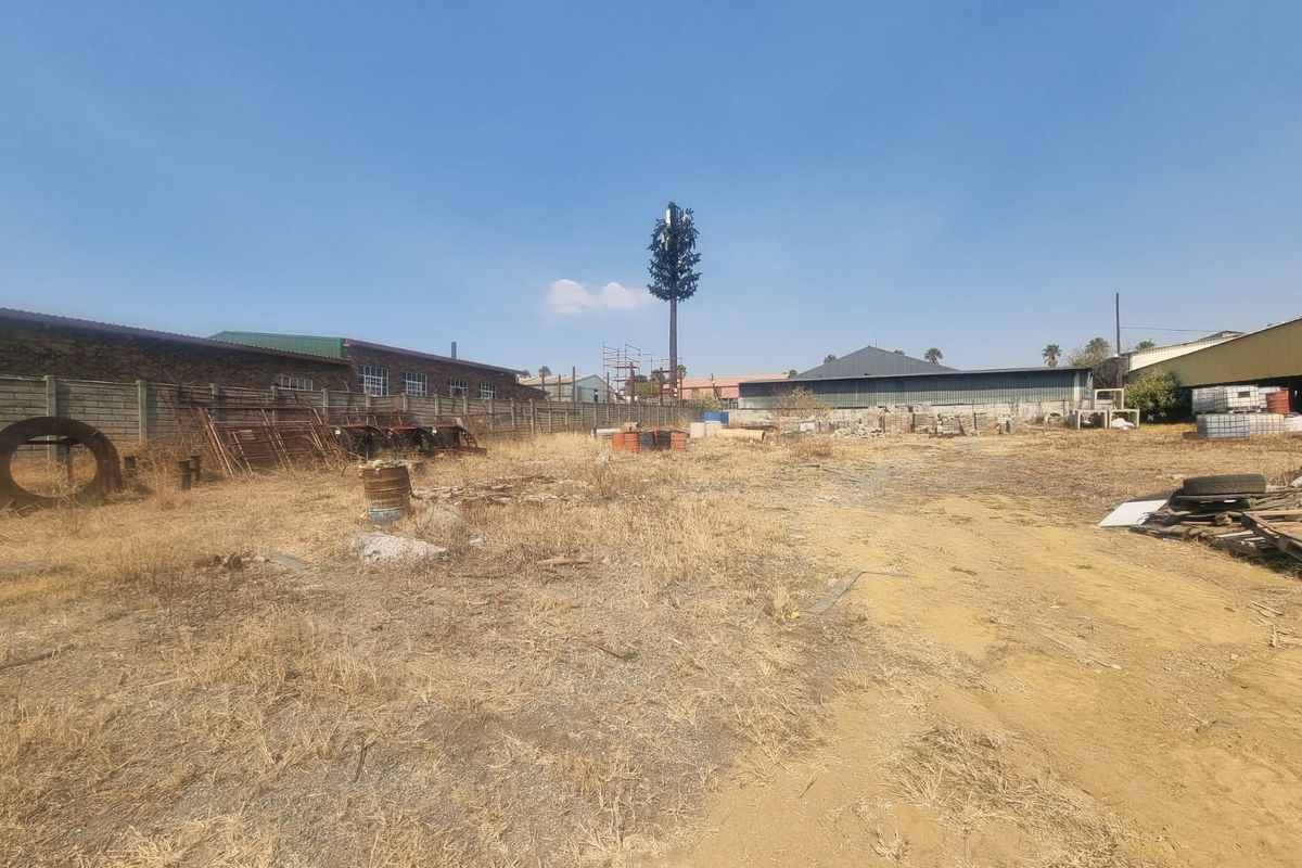 A vacant commercial land plot featuring a perimeter wall and a telecommunications mast, currently showing signs of neglect and debris.