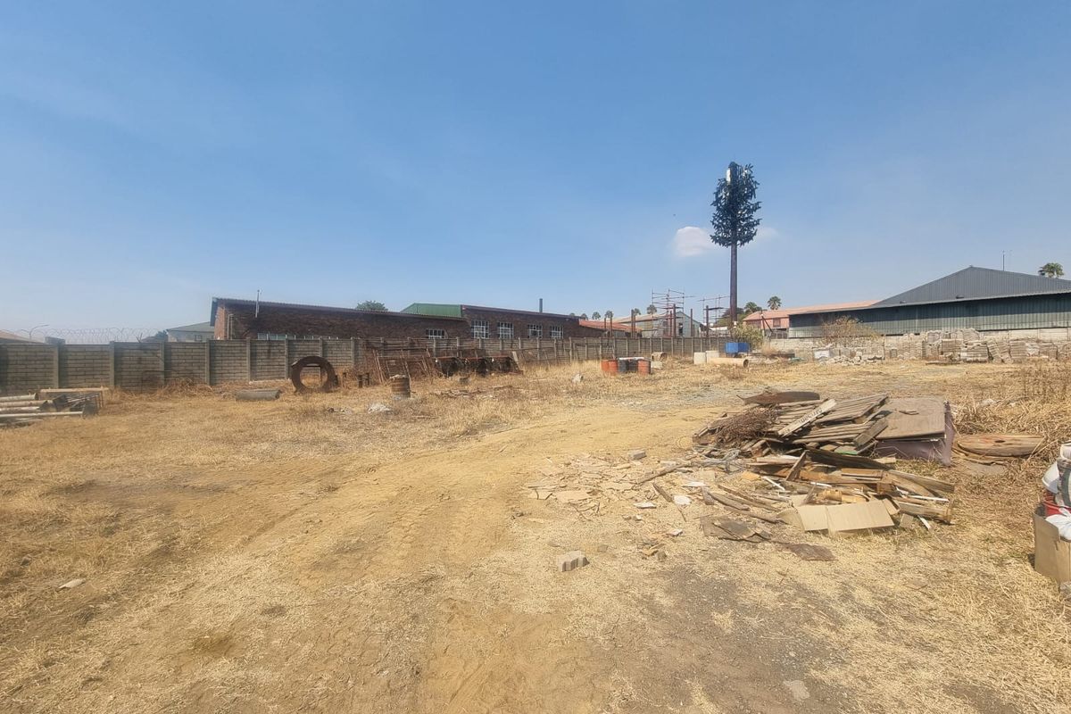 Vacant commercial land featuring a perimeter wall and a telecommunications mast, currently containing scattered debris and dry vegetation.