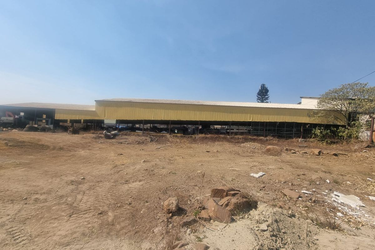 View of a large open-sided commercial warehouse structure with corrugated metal roofing situated on an undeveloped dirt lot.