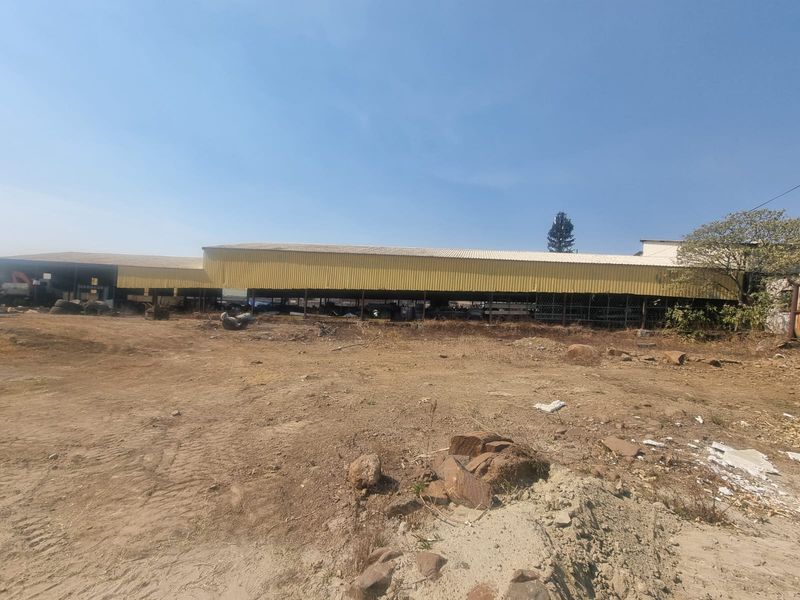 View of a large open-sided commercial warehouse structure with corrugated metal roofing situated on an undeveloped dirt lot.