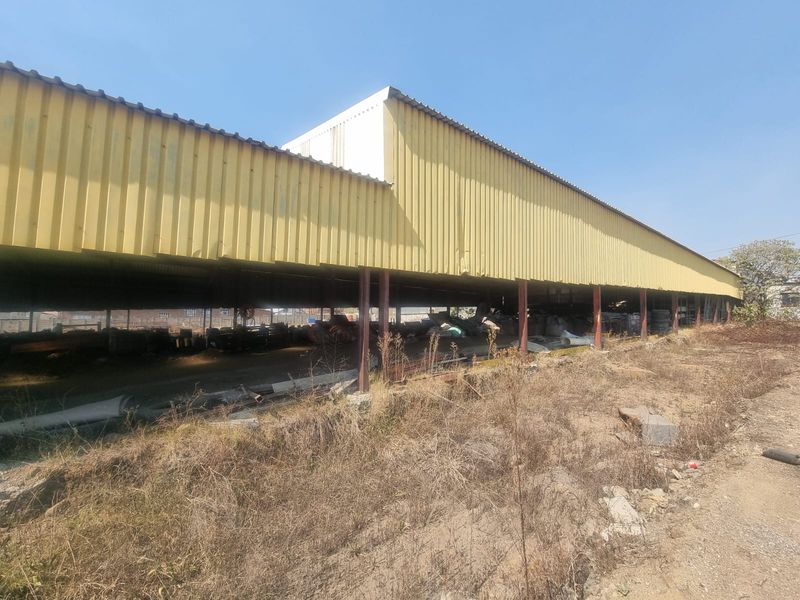 Large industrial storage shed featuring corrugated metal cladding and steel support columns, currently showing signs of significant wear and exterior debris.