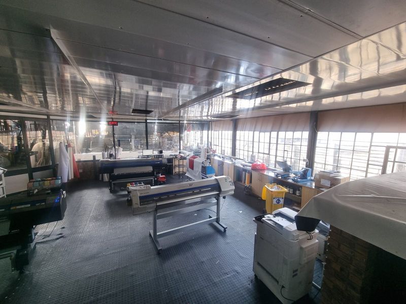 A functional commercial utility or production space featuring industrial rubber flooring, extensive window frontage, and built-in work counters suitable for printing or manufacturing operations.