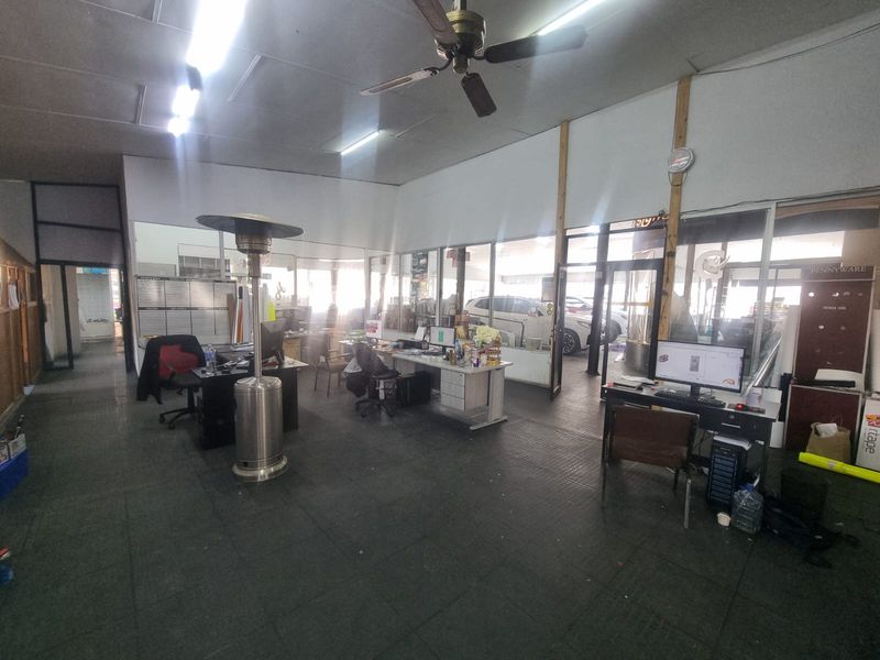 Open-plan commercial office space featuring glass partitions, industrial rubber flooring, and overhead fluorescent lighting, suitable for a professional workspace.