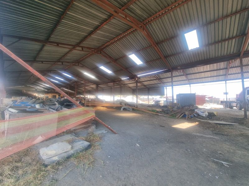 Large open-plan industrial utility space featuring a high corrugated metal roof with integrated skylights and a dirt floor, suitable for storage or workshop use.
