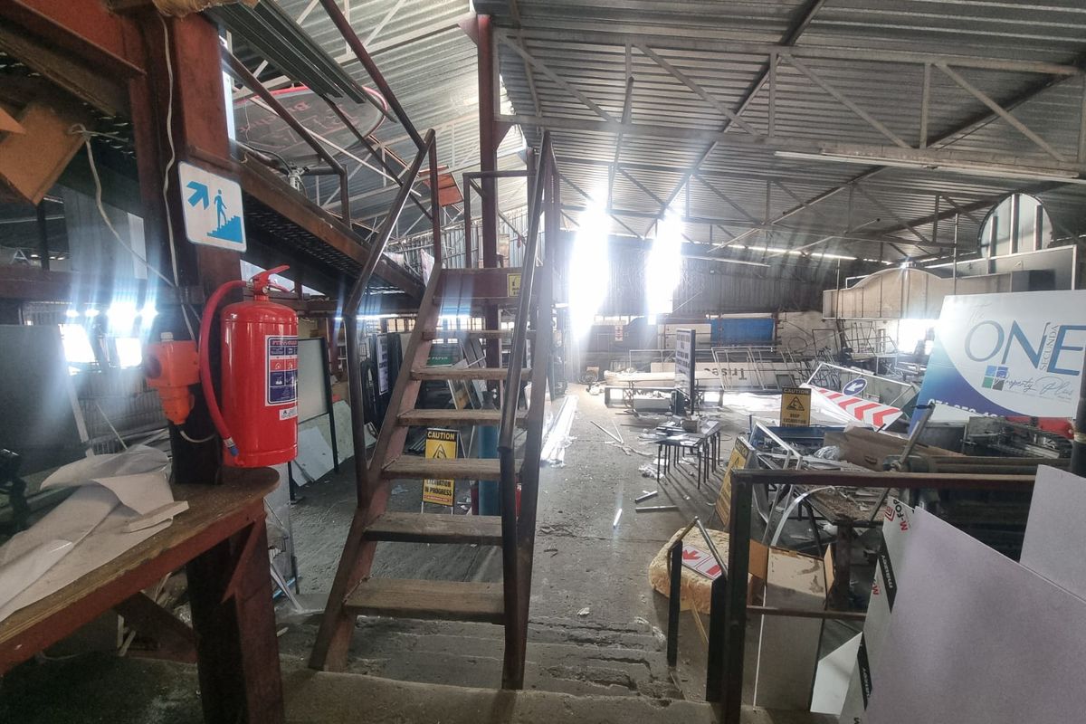 Industrial utility space featuring exposed steel roof trusses, a metal staircase, and concrete flooring, suitable for storage or workshop use.