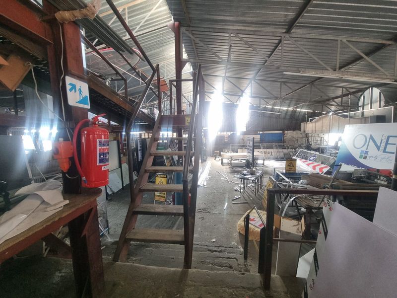 Industrial utility space featuring exposed steel roof trusses, a metal staircase, and concrete flooring, suitable for storage or workshop use.