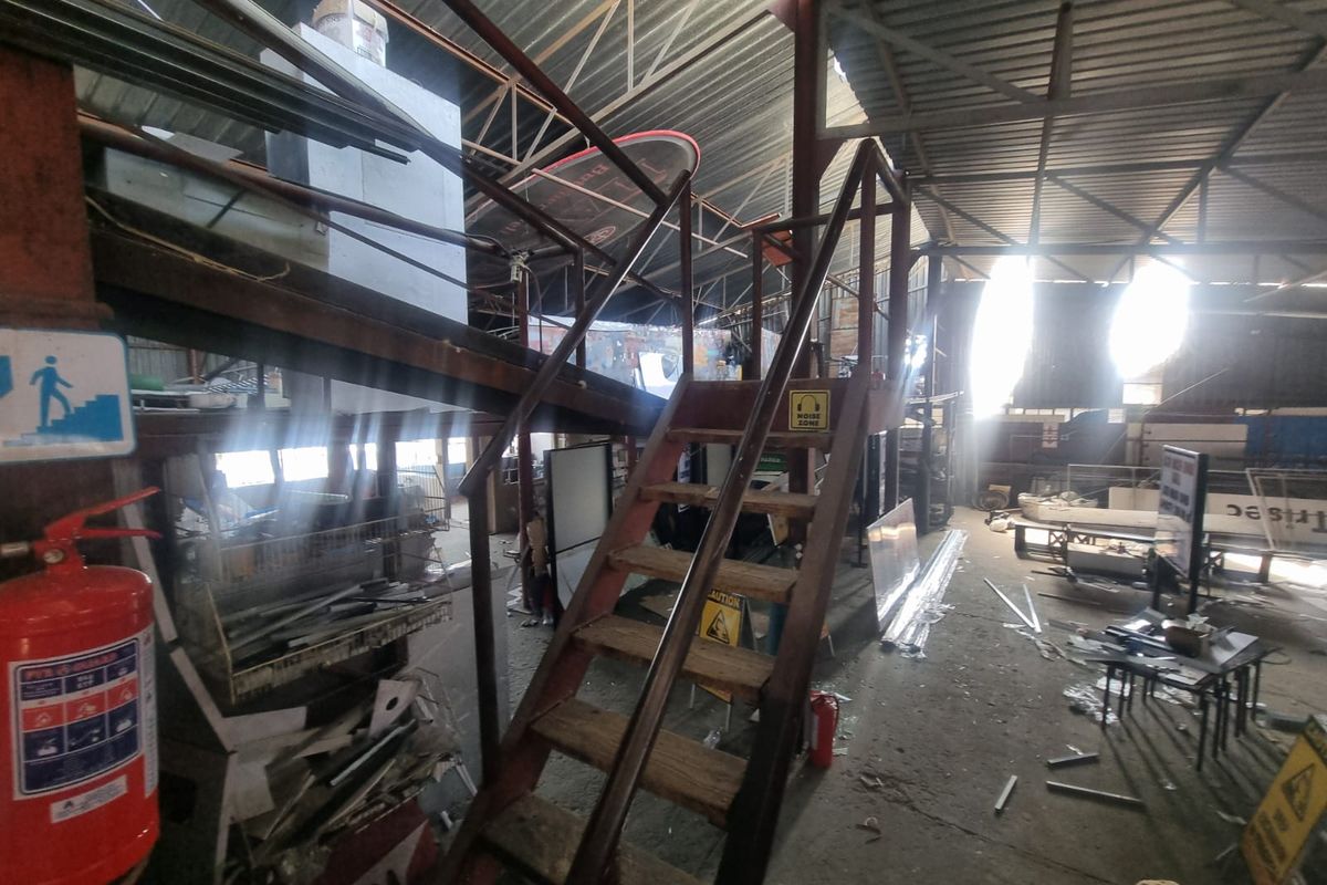 Industrial utility space featuring exposed steel roof trusses, a metal staircase, and concrete flooring, suitable for storage or workshop operations.