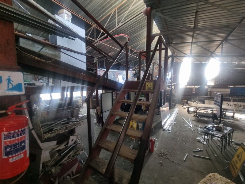 Industrial utility space featuring exposed steel roof trusses, a metal staircase, and concrete flooring, suitable for storage or workshop operations.