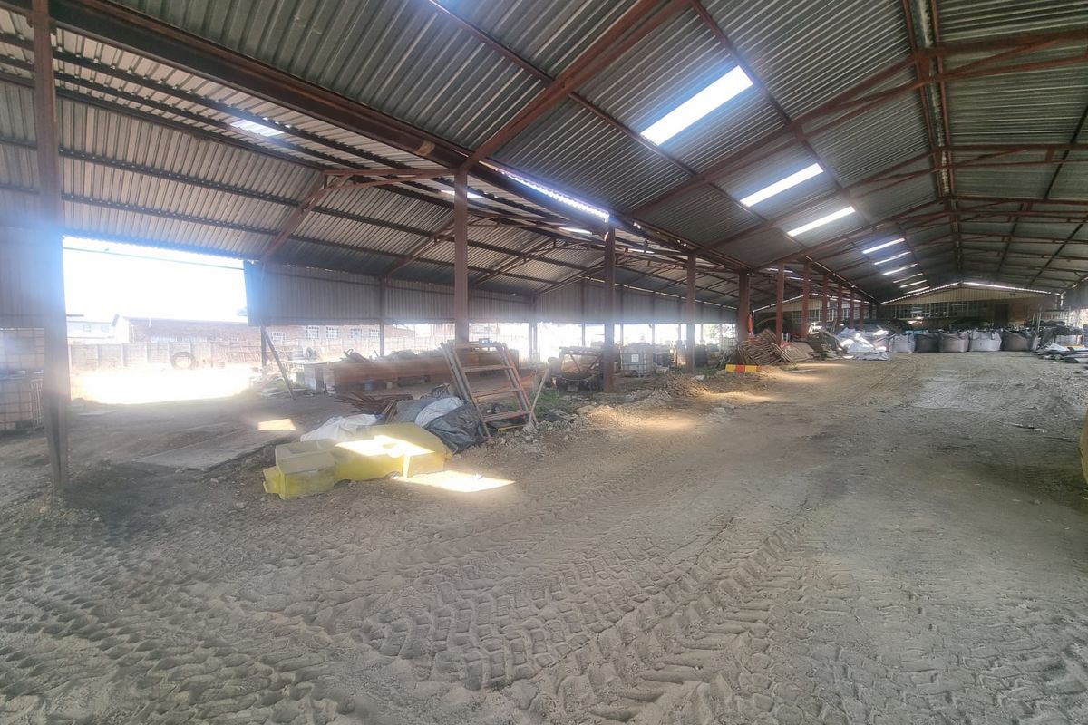 Large open-plan industrial utility space featuring a steel frame structure, corrugated metal roofing with integrated skylights, and an unpaved dirt floor.