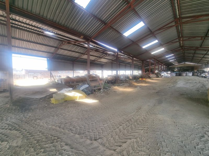 Large open-plan industrial utility space featuring a steel frame structure, corrugated metal roofing with integrated skylights, and an unpaved dirt floor.