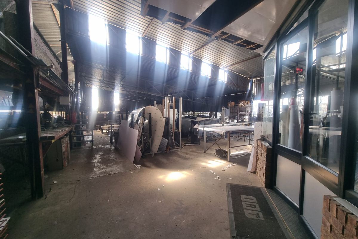 Industrial utility space featuring exposed steel roof structure, corrugated metal roofing, skylights, and concrete flooring with an adjacent glass-partitioned office area.