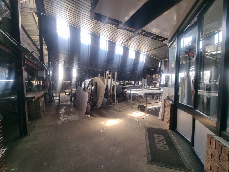 Industrial utility space featuring exposed steel roof structure, corrugated metal roofing, skylights, and concrete flooring with an adjacent glass-partitioned office area.