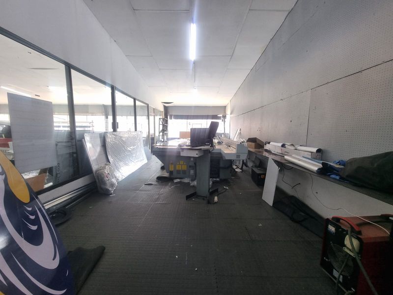 A commercial utility or workshop space featuring large glass storefront windows, rubber flooring, and drop ceiling lighting, suitable for various industrial or retail applications.