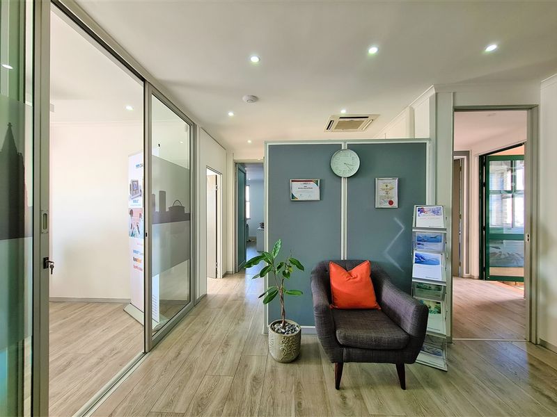 A modern office reception area featuring glass partitions, laminate flooring, recessed lighting, and a central partition wall with integrated air conditioning.