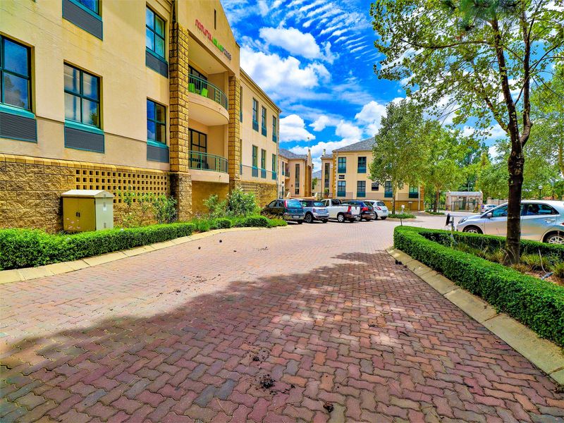 A well-maintained office complex exterior featuring a paved driveway, landscaped garden borders, and multi-story building facades with integrated balconies.