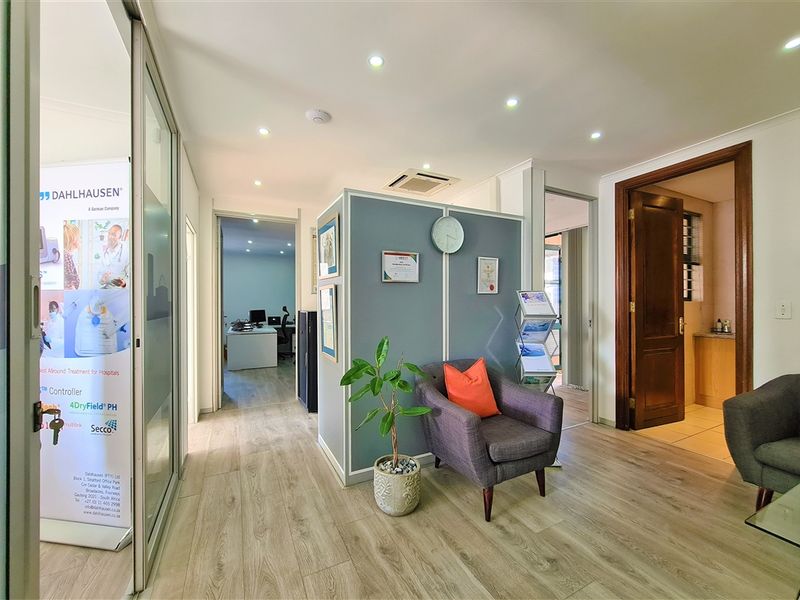 A professional office reception area featuring laminate flooring, recessed lighting, and a central partition wall leading to multiple private office spaces.